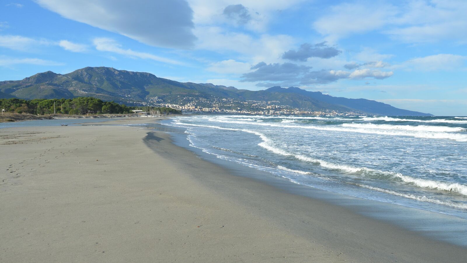 A quiet sandy beach with waves and coastal mountains